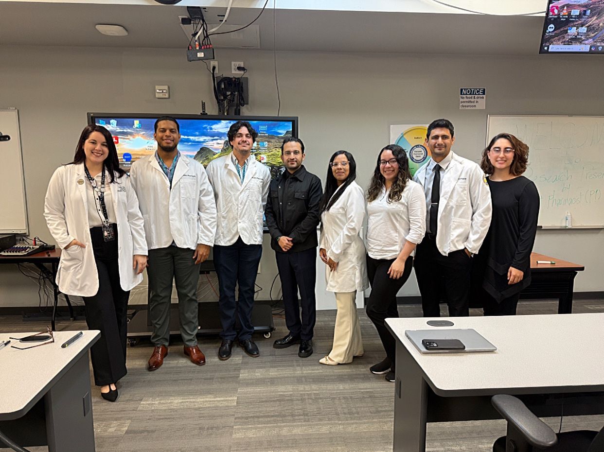 A group of PharmD students and faculty members at Larkin University College of Pharmacy posing in a classroom after research presentations, with some students wearing lab coats.